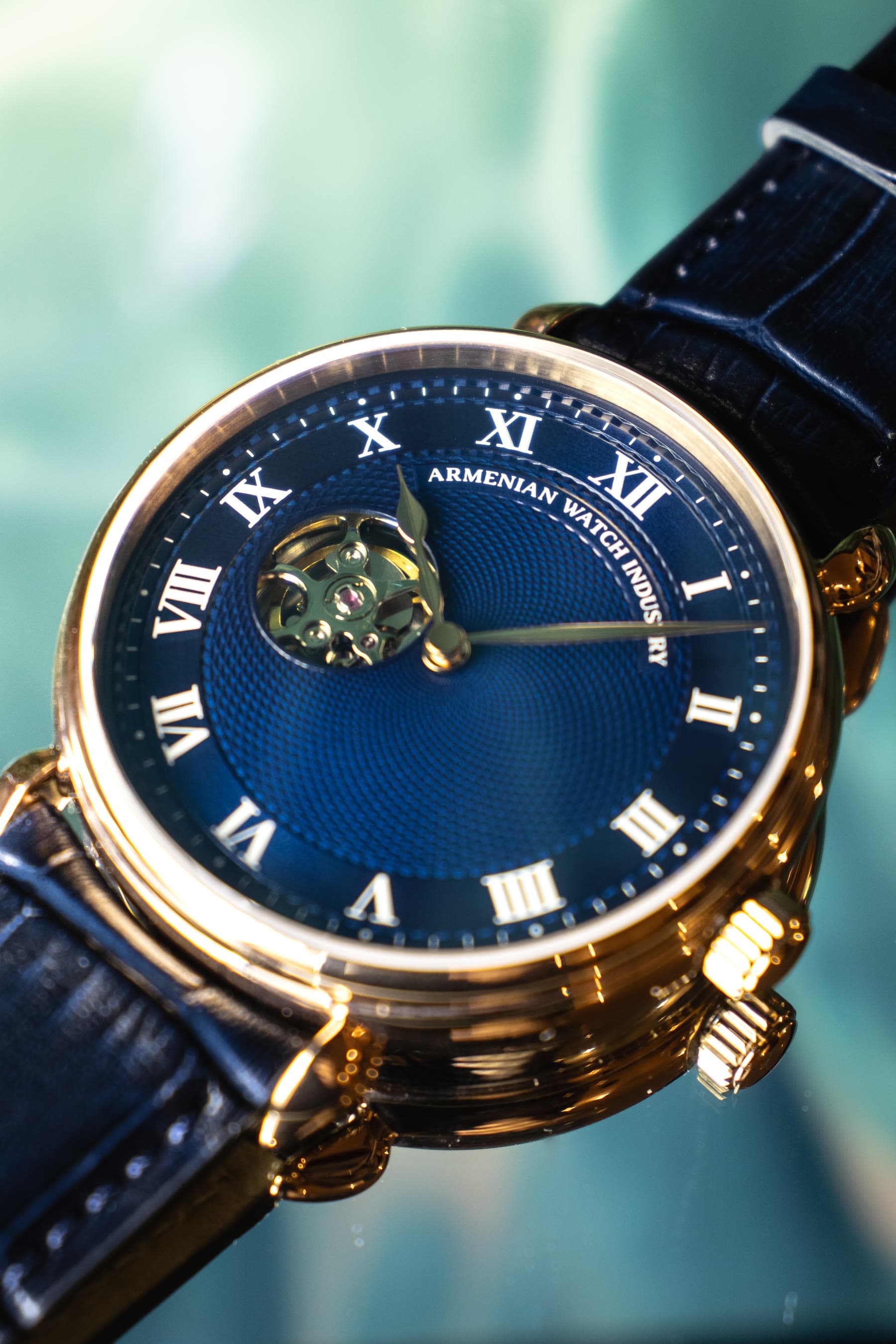 A gold AWI watch with a blue dial on a leather strap