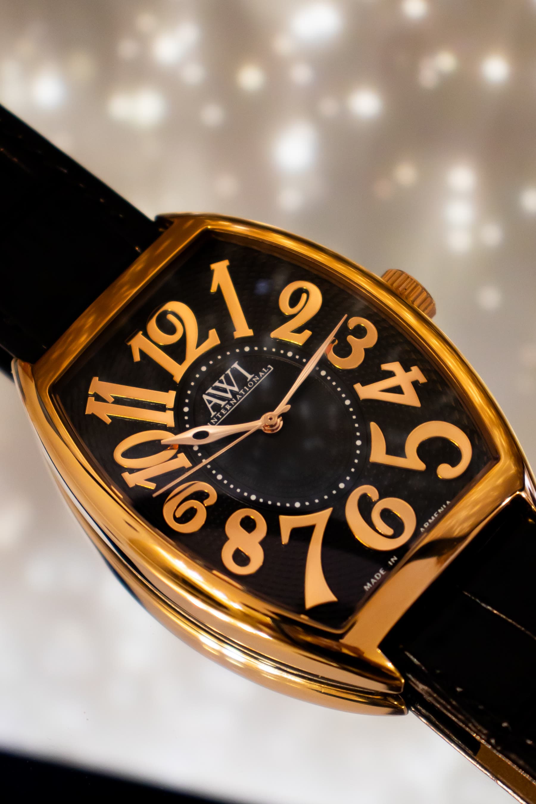 A gold tonneau AWI watch with a white dial