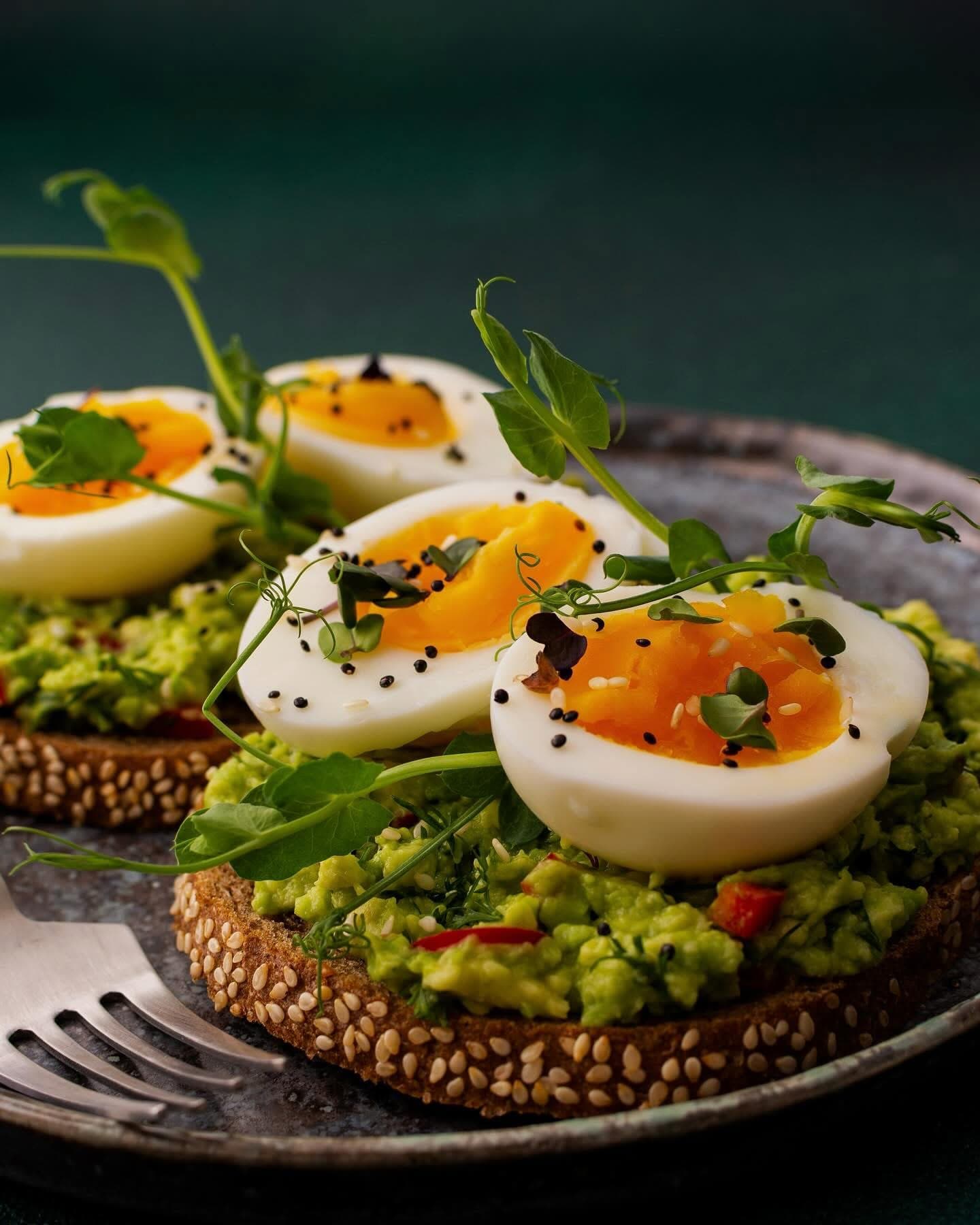 Toast with avocado, eggs and microgreens on a dark plate