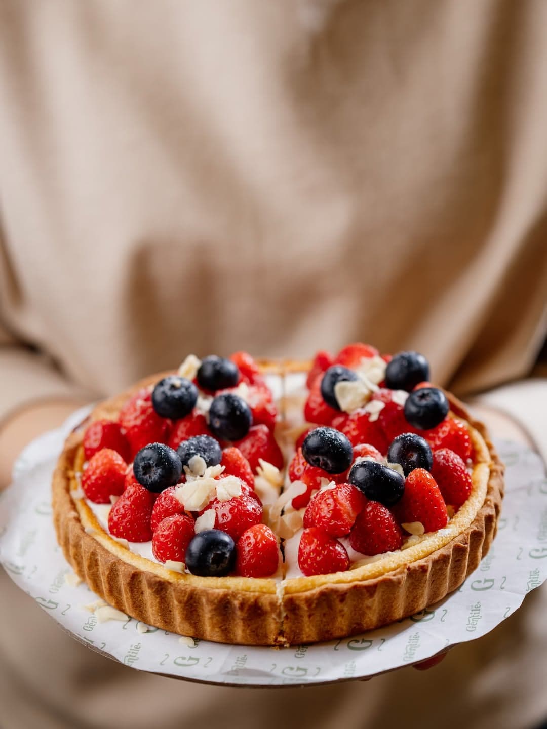 A tart with raspberries, blueberries and almonds held in both hands
