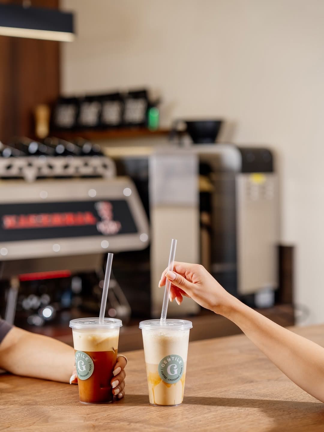Two iced coffees in branded Gentile cups by the espresso machine