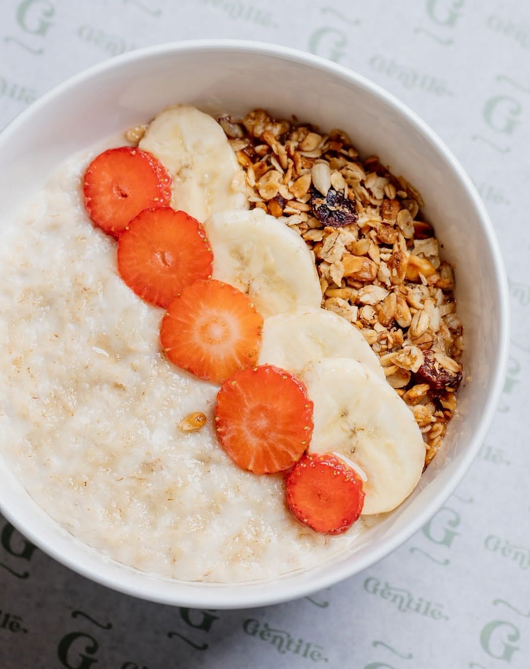 Porridge with strawberries, banana and granola in a branded bowl
