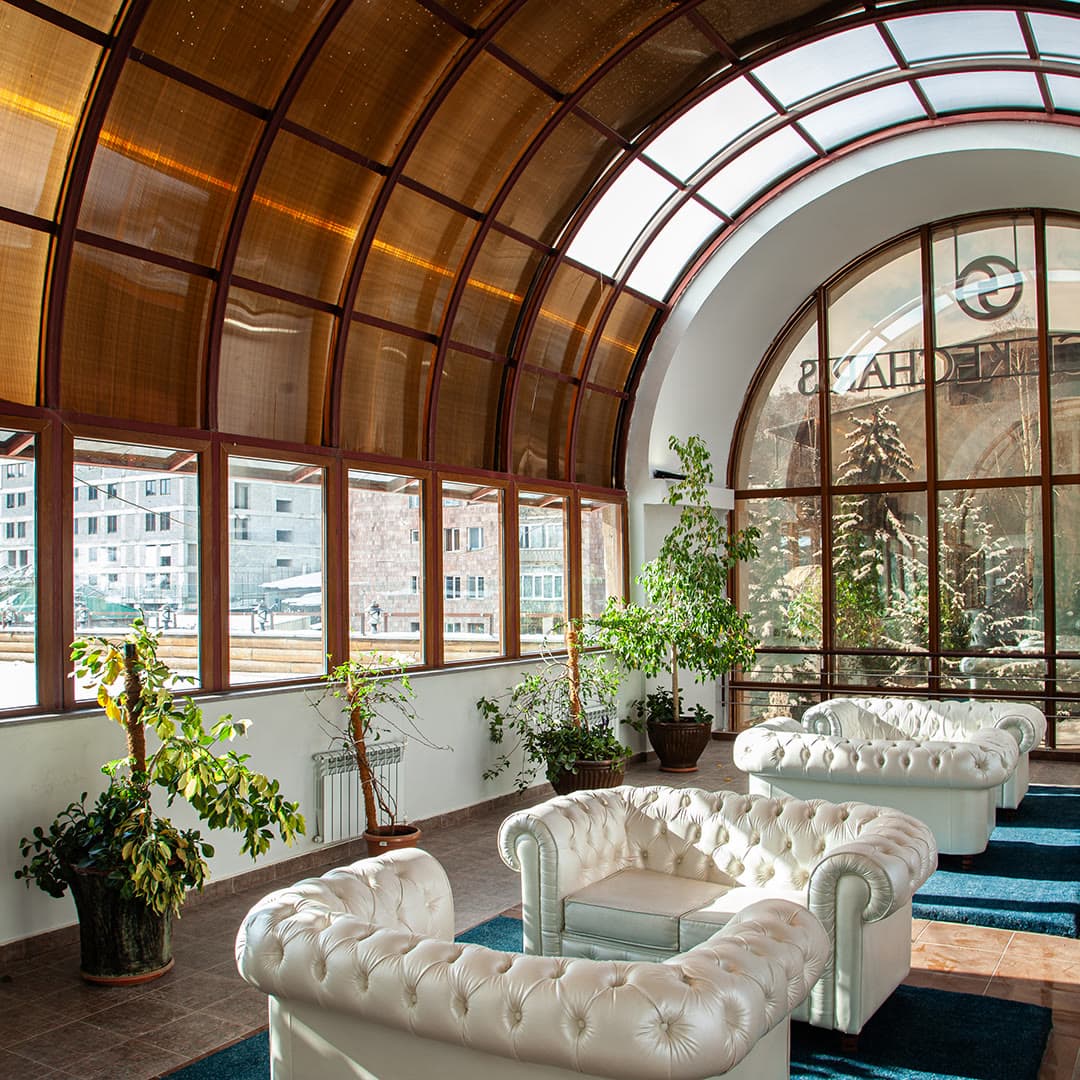 The panoramic atrium of Grace Kecharis: white chesterfield armchairs under a glass vault with a view of Tsaghkadzor