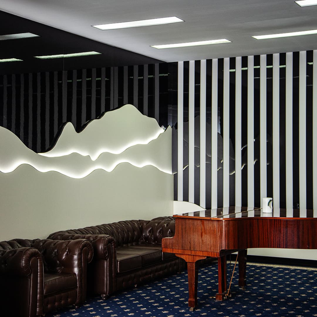 A dark lounge with a neon mountain silhouette, leather sofas and a grand piano