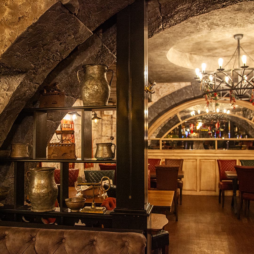 The hotel restaurant under stone vaults with copper ware and wrought-iron chandeliers