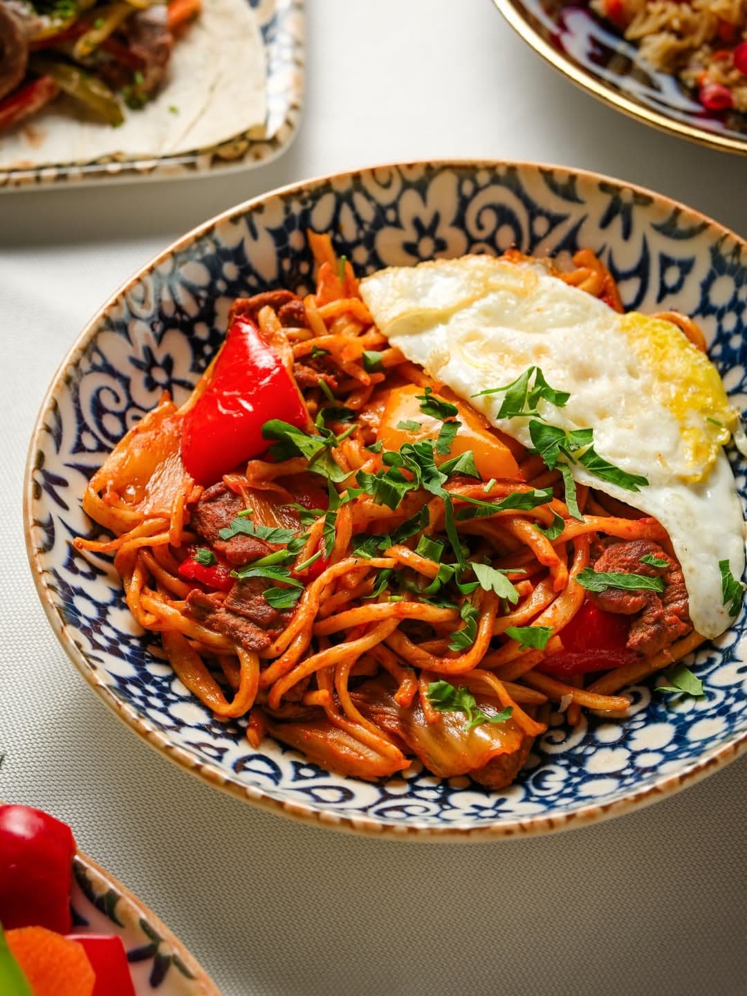 Lagman with a fried egg and bell pepper in an Uzbek bowl