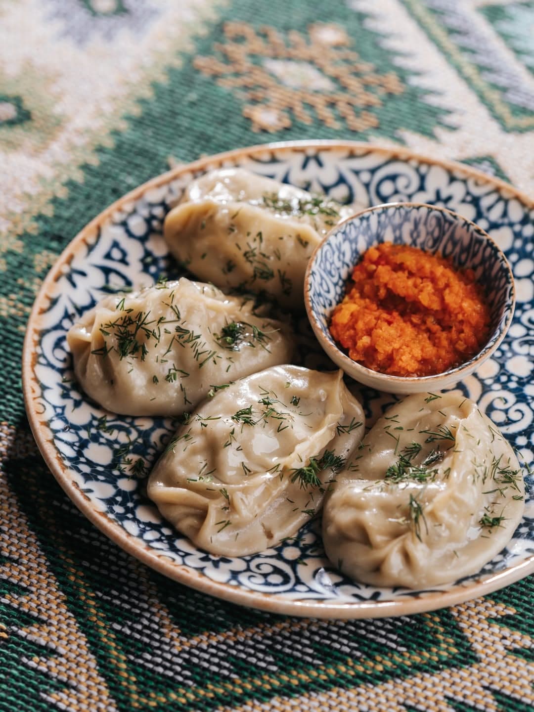 Manti with hot sauce on Uzbek tableware over a suzani cloth