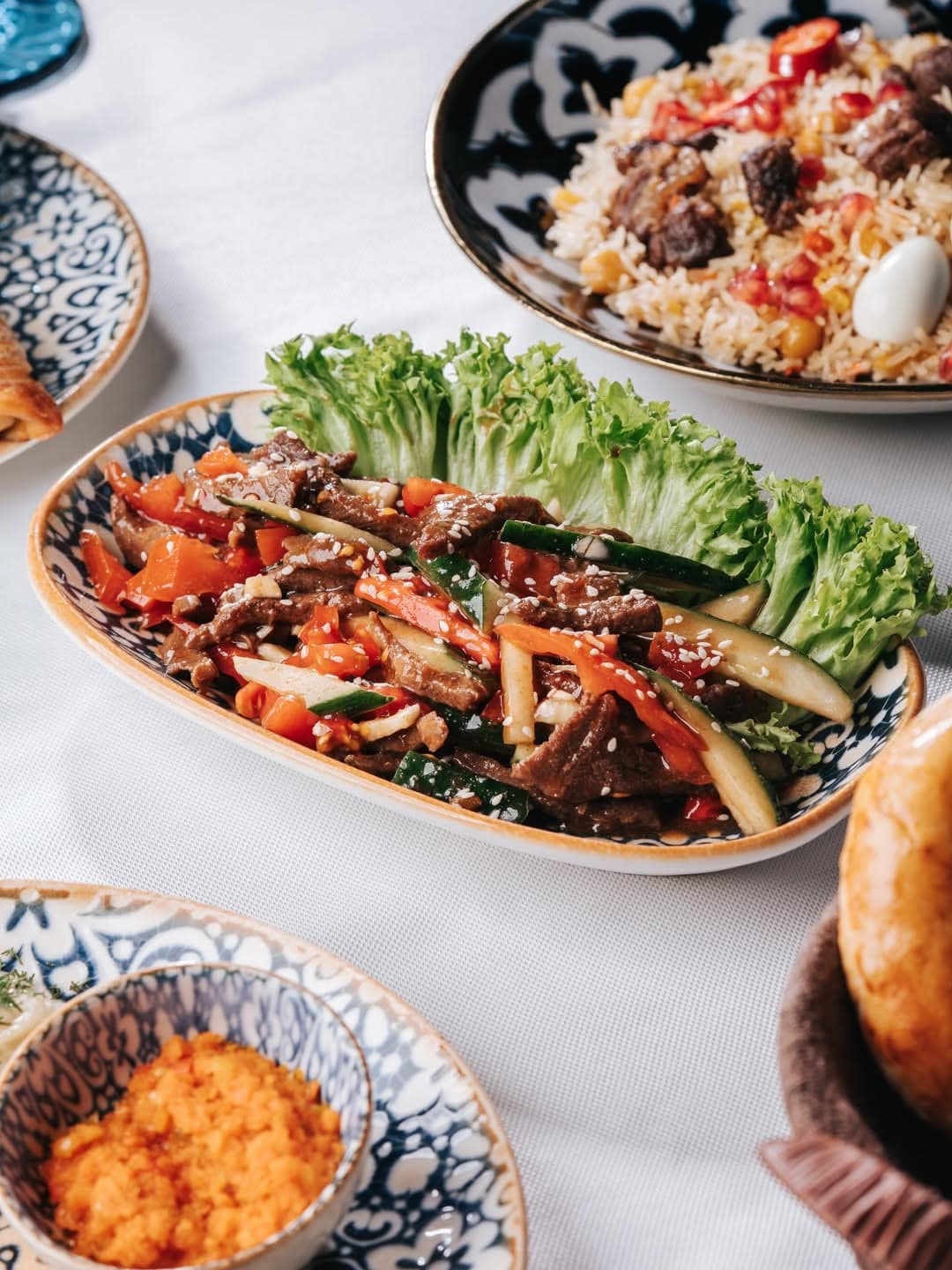A laid table: plov, meat salads and herbs